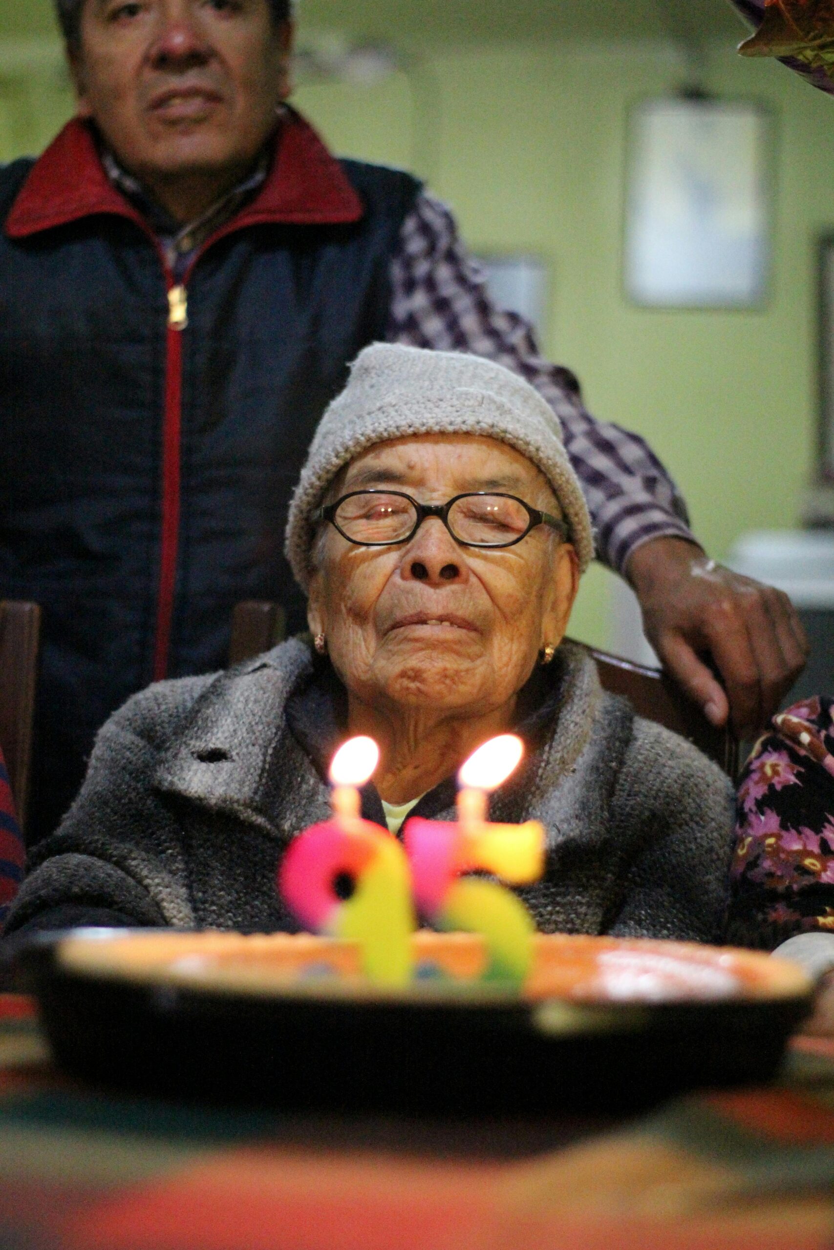 A senior woman celebrates her 95th birthday with a cake and candles indoor setting.